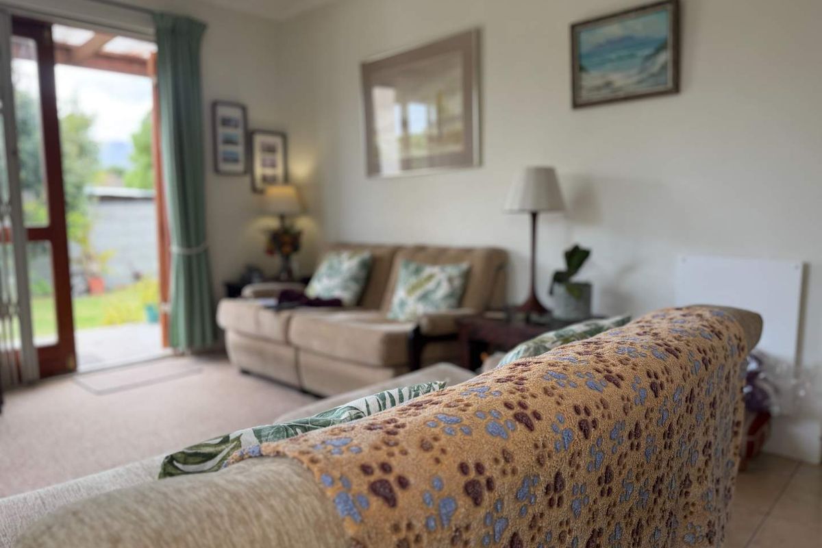 A comfortable living room featuring tiled and carpeted flooring with direct access to an outdoor patio area through a glass sliding door.