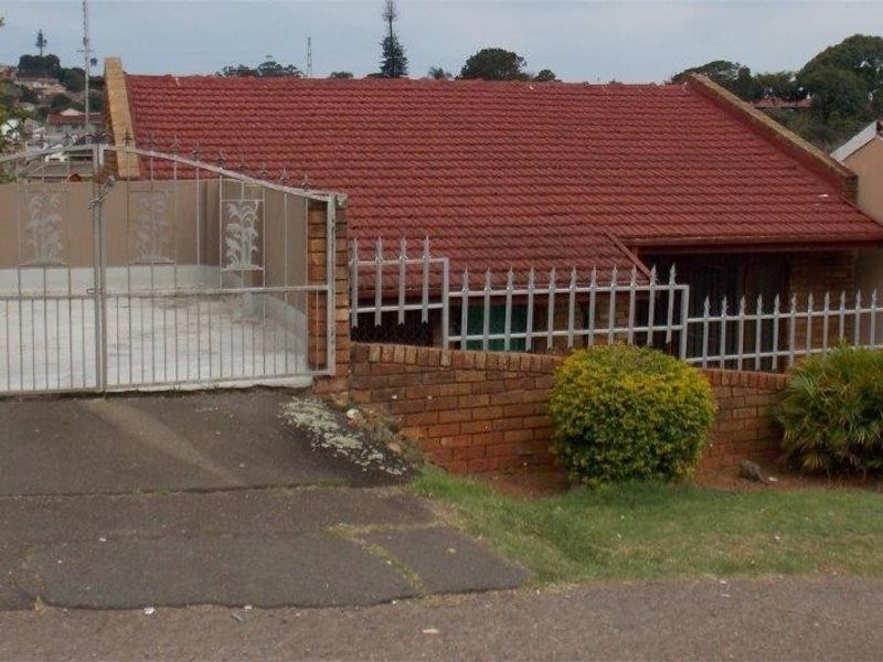 Front elevation of a residential house featuring a red tiled roof, brick boundary wall, and a gated driveway entrance.