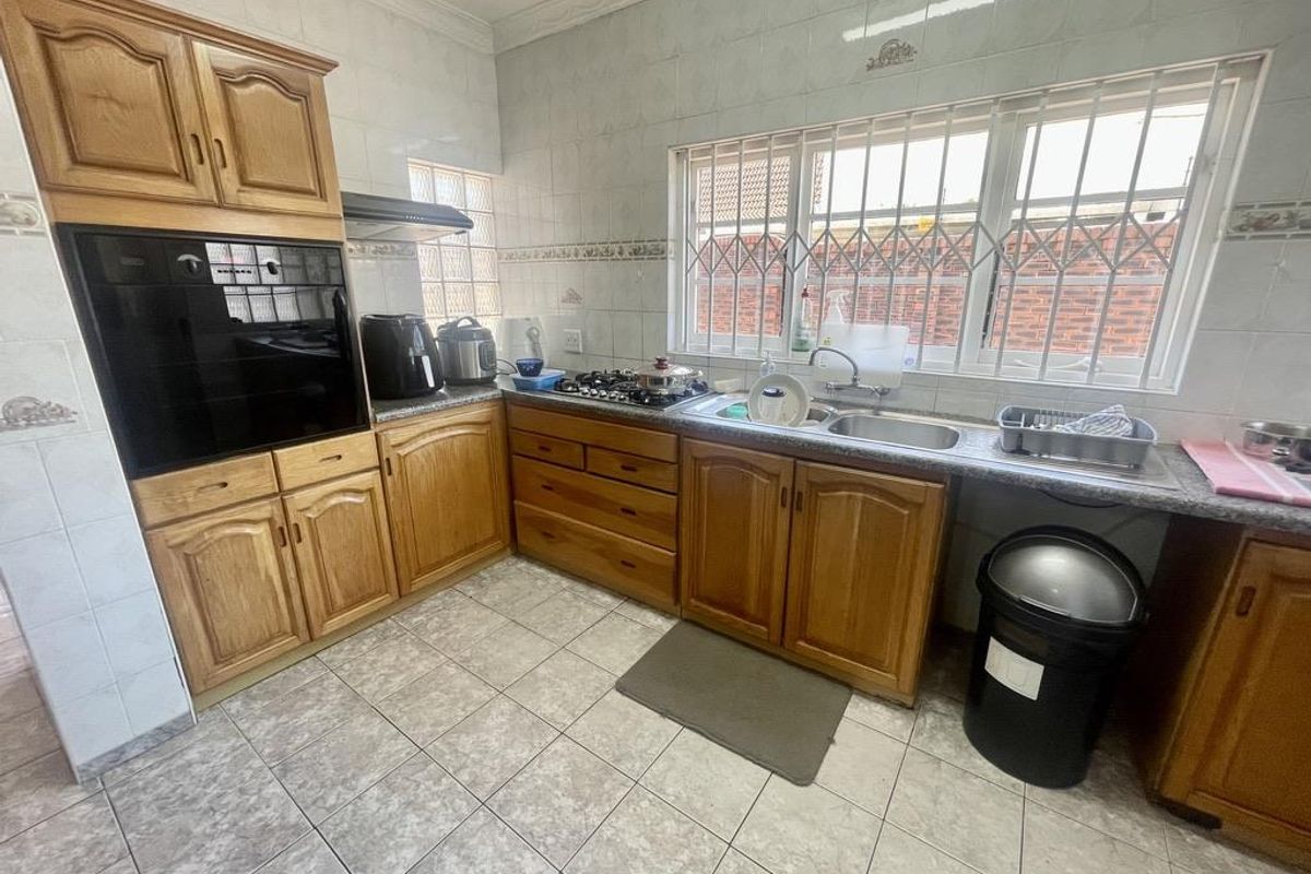 A functional kitchen featuring wooden cabinetry, a built-in oven, gas hob, and a double-basin sink with tiled splashbacks and flooring.