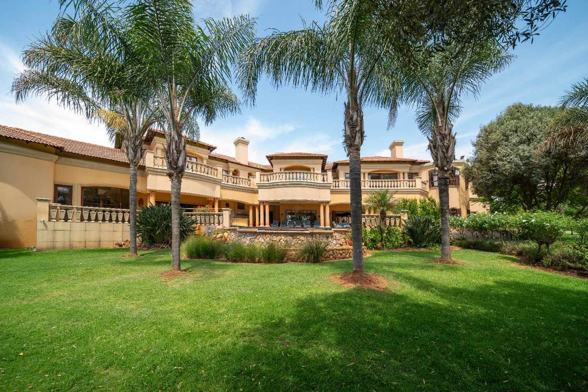 A spacious rear elevation of a large residence featuring a landscaped garden, mature palm trees, and a stone-clad swimming pool area with multiple balconies.
