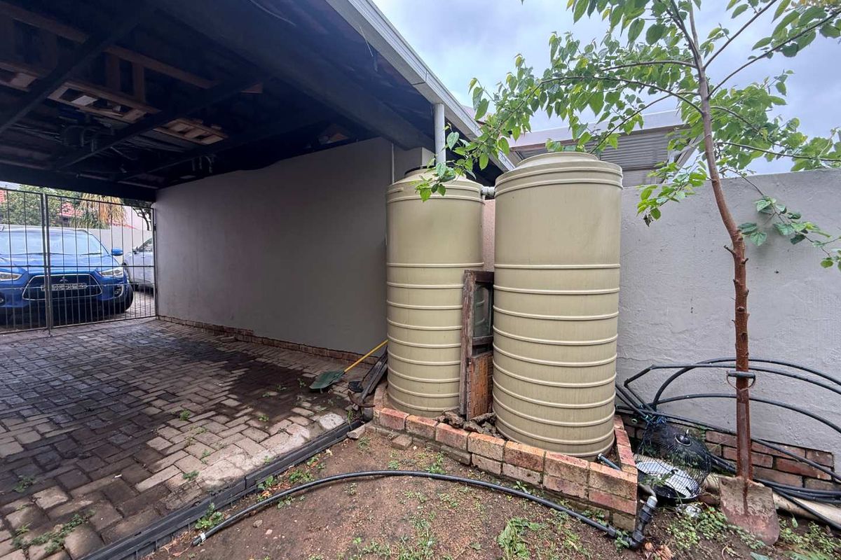 Rear exterior area featuring two large water storage tanks, a covered carport, and brick paving.