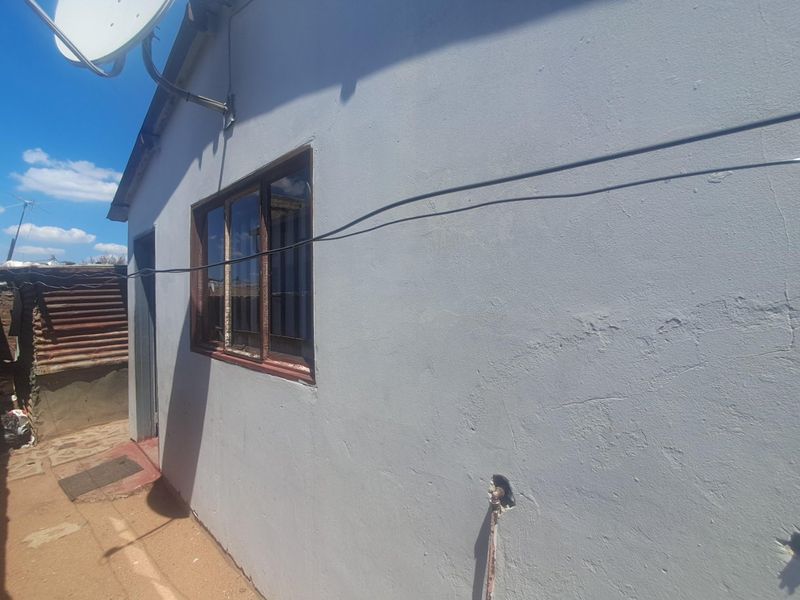 A view of the rear exterior wall showing a satellite dish, a metal-framed window, and an external water tap with visible plaster cracking.