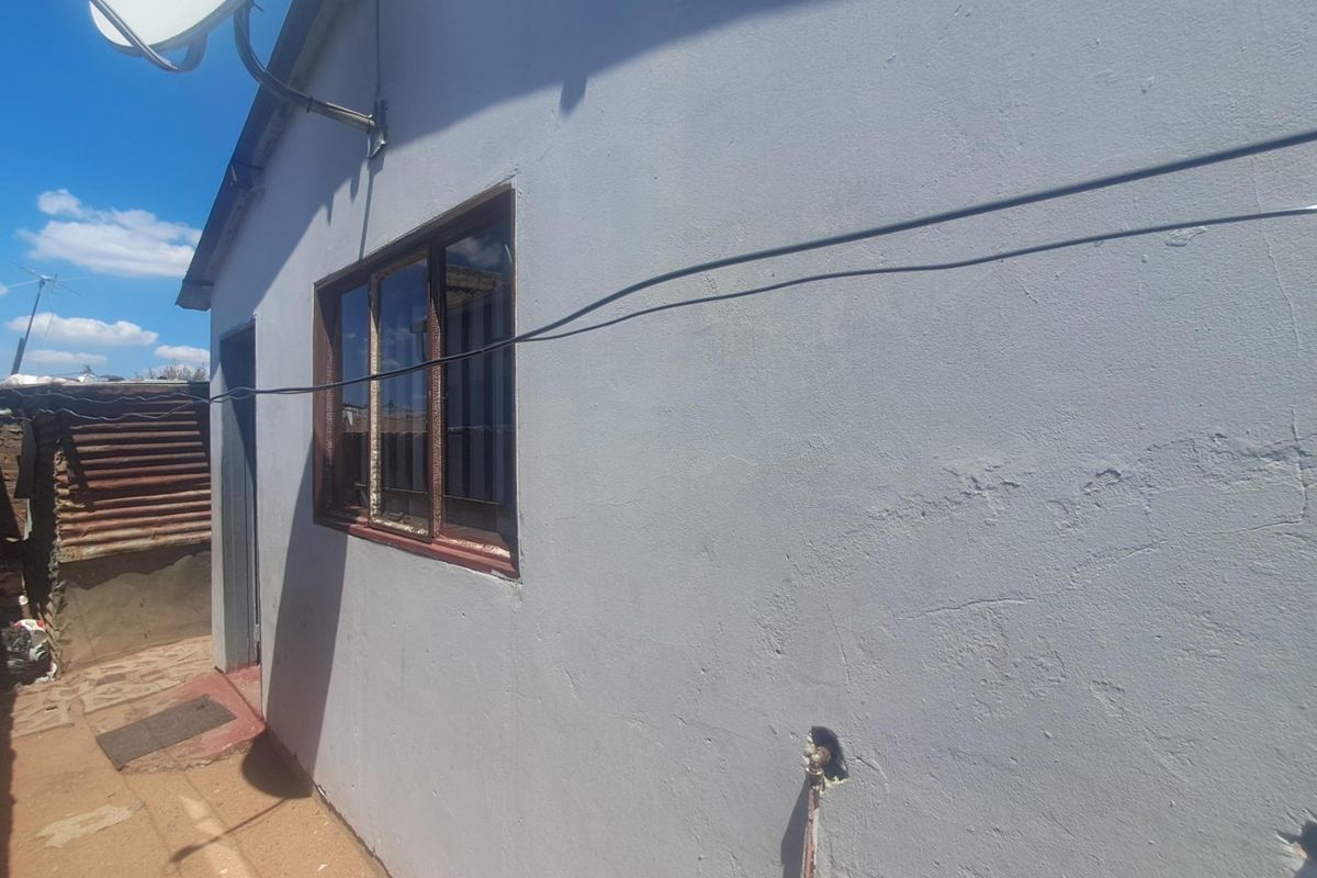 A view of the rear exterior wall showing a satellite dish, a metal-framed window, and an external water tap with visible plaster cracking.