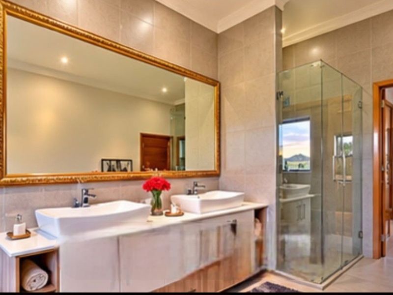 Modern bathroom featuring a double vanity with vessel sinks, a large framed mirror, and a glass-enclosed shower with neutral wall tiling.
