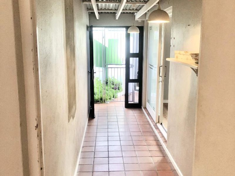 A narrow hallway featuring tiled flooring, exposed timber rafters with a corrugated roof, and direct access to an outdoor area through a security gate.