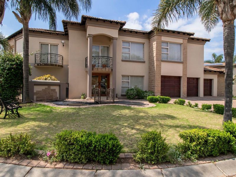 Front elevation of a double-story residential house featuring stone cladding, wrought iron balcony railings, and a well-maintained garden with a paved driveway.
