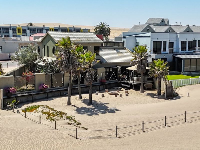 Aerial view of a coastal property featuring a tiled roof, boundary walls, and a raised timber deck situated directly on the sandy beach.