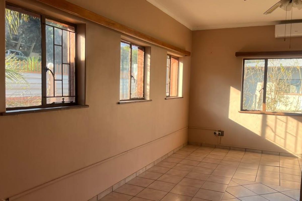 An empty living room featuring tiled flooring, a ceiling fan, wall-mounted air conditioning, and large windows with security bars.