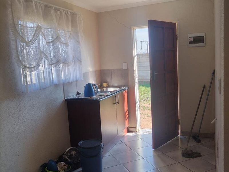 A functional scullery area featuring tiled flooring, built-in base cabinetry with a sink, and direct access to the exterior.