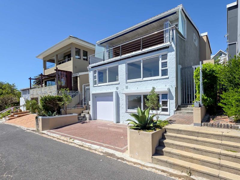 Front elevation of a multi-level residential property featuring a paved driveway, integrated garage, and an upper-level balcony with metal railings.
