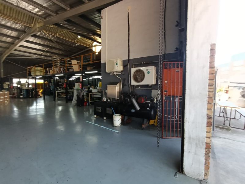 Industrial warehouse space featuring a mezzanine level, exposed steel roof structure, epoxy flooring, and integrated air conditioning and compressor systems.