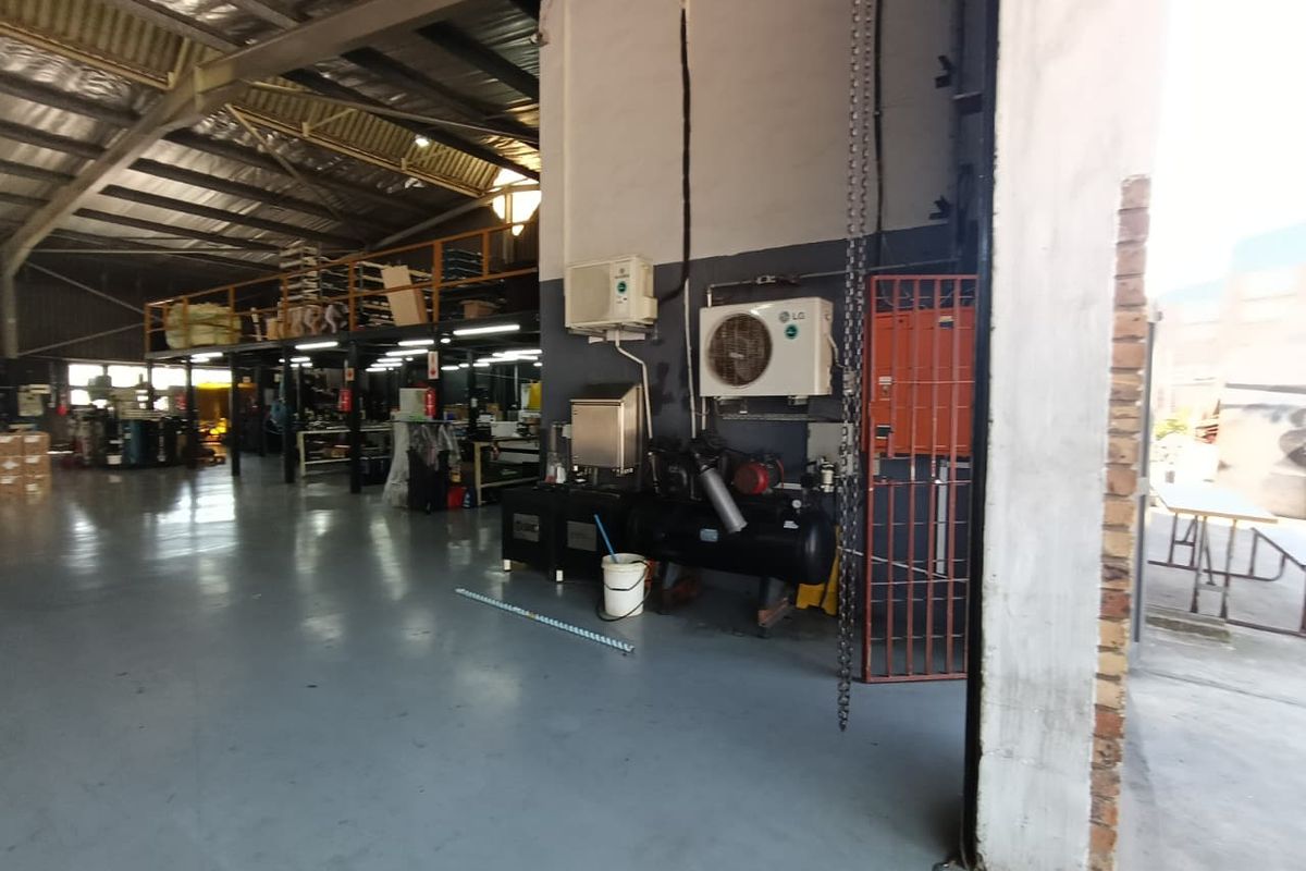 Industrial warehouse space featuring a mezzanine level, exposed steel roof structure, epoxy flooring, and integrated air conditioning and compressor systems.