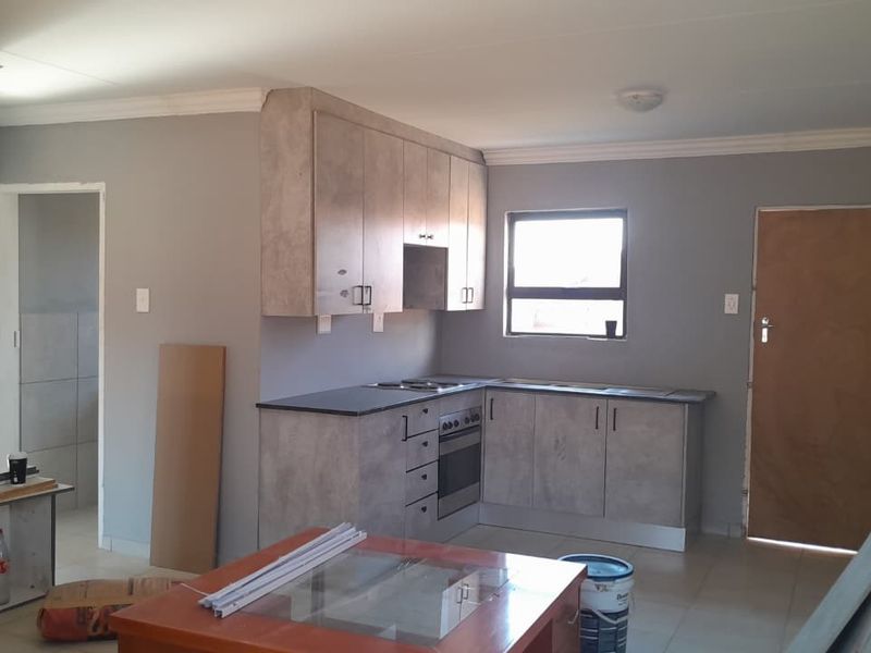 A functional kitchen space featuring modern grey cabinetry, built-in oven and hob, and tiled flooring, currently in a state of completion.