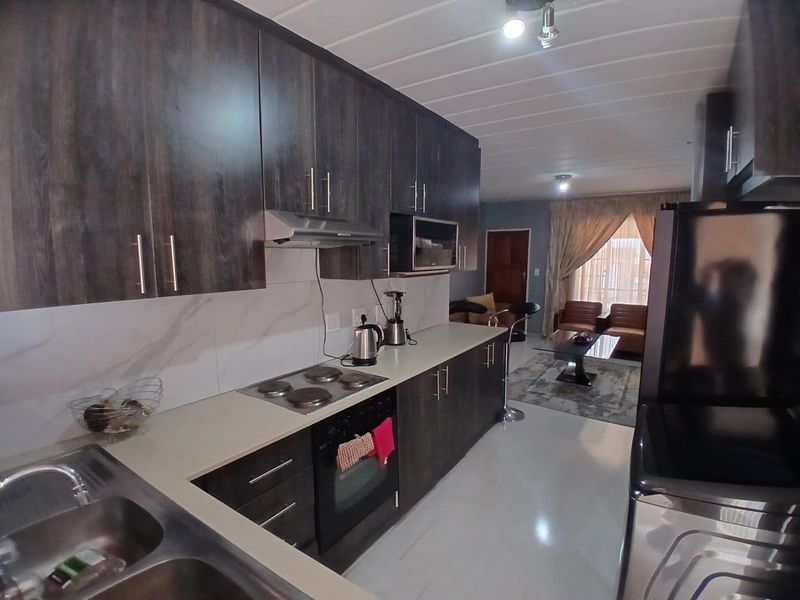 Open-plan kitchen featuring dark wood cabinetry, integrated appliances, and a marble-look splashback, flowing seamlessly into the adjacent living area.