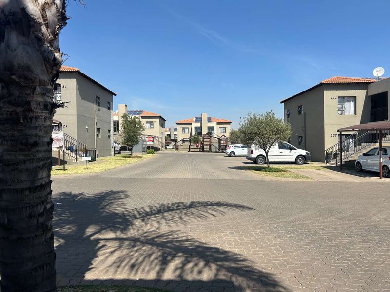 A view of the townhouse complex street and driveway, featuring paved surfaces, multi-story residential blocks, and dedicated carport parking areas.