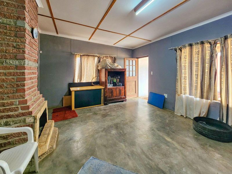 Living room featuring an exposed brick fireplace, concrete flooring, and timber ceiling beams, offering a rustic foundation for renovation.