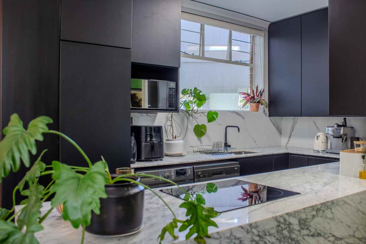 Modern kitchen featuring sleek black cabinetry, premium marble countertops and backsplash, integrated induction hob, and built-in appliances for a sophisticated, high-end finish.