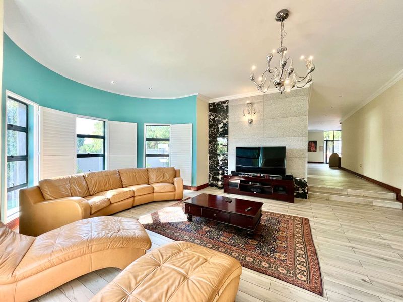 Spacious living room featuring a curved wall, tiled flooring, plantation shutters, and a decorative feature wall with integrated lighting.