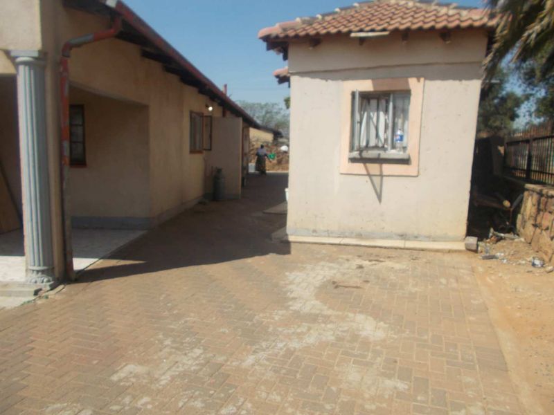 Rear exterior view of the property featuring a paved courtyard area between two structures with tiled roofing and security window bars.