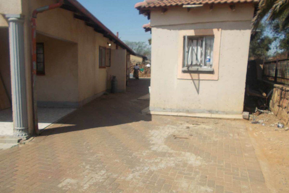 Rear exterior view of the property featuring a paved courtyard area between two structures with tiled roofing and security window bars.