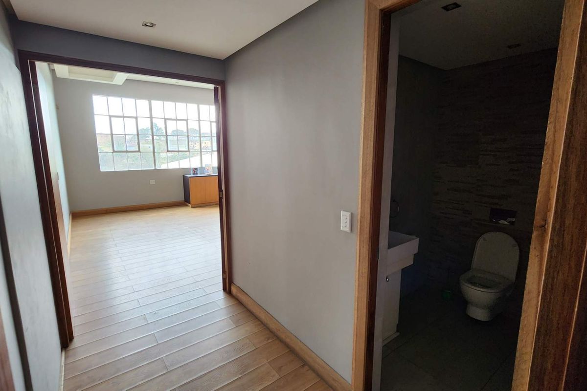 A clean hallway featuring laminate flooring and wooden door frames, providing access to an adjacent office space and a bathroom.