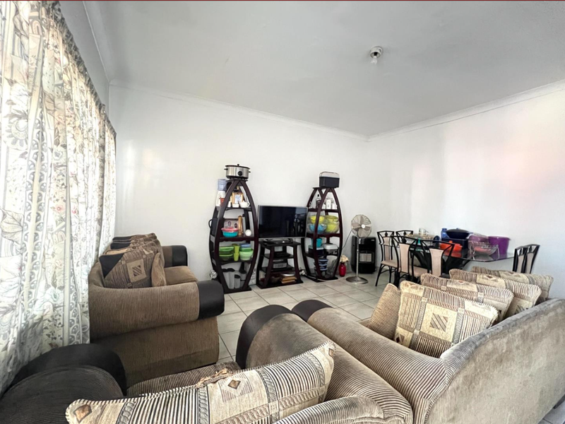 A spacious living area featuring neutral tiled flooring and coved cornicing, offering a functional layout suitable for comfortable seating and dining arrangements.