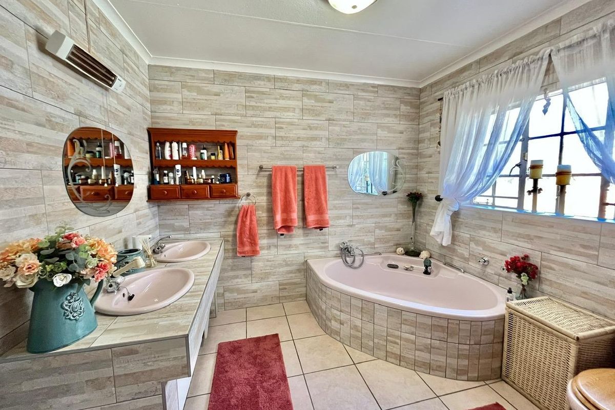 A spacious bathroom featuring a built-in corner bathtub, dual vanity sinks with tiled countertops, and neutral wall tiling throughout.