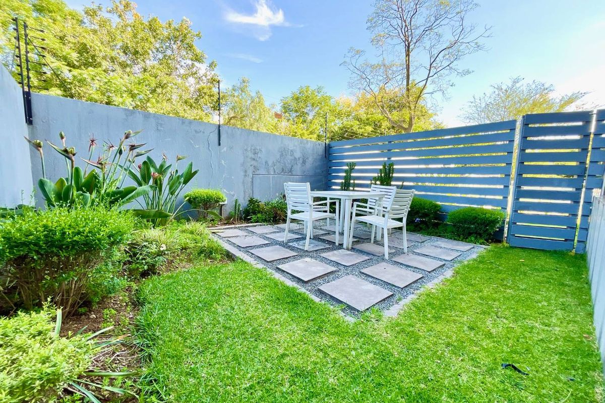 A private rear garden featuring a paved patio area, manicured lawn, and secure perimeter fencing with integrated electric security wiring.