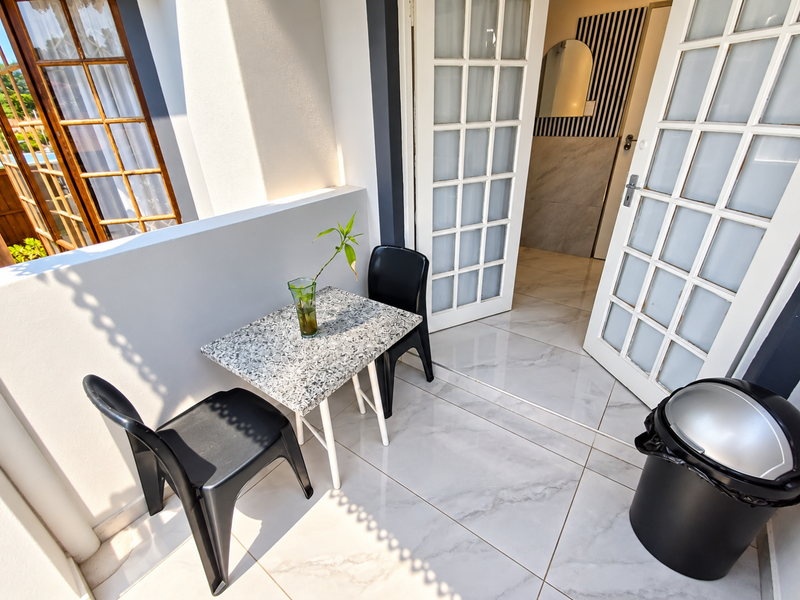 A bright balcony area featuring modern tiled flooring and classic white french doors leading into the interior space.