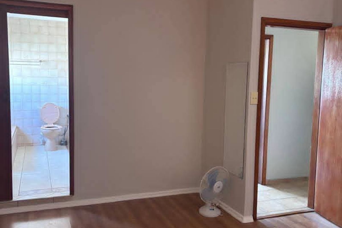 A vacant bedroom featuring laminate flooring, a ceiling fan, and direct access to an adjoining bathroom.