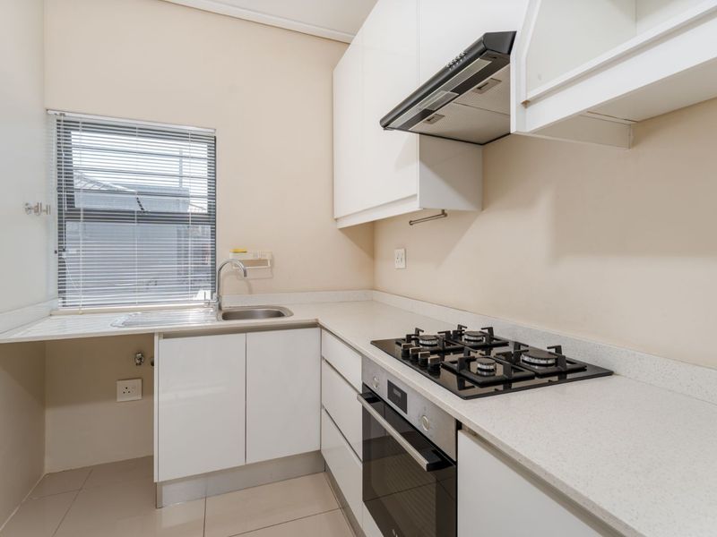 A clean, modern kitchen featuring white cabinetry, stone countertops, a gas hob, built-in oven, and an integrated sink with a window view.