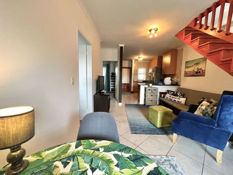 Open plan living area featuring tiled flooring and a wooden staircase, seamlessly connecting to the kitchen space.