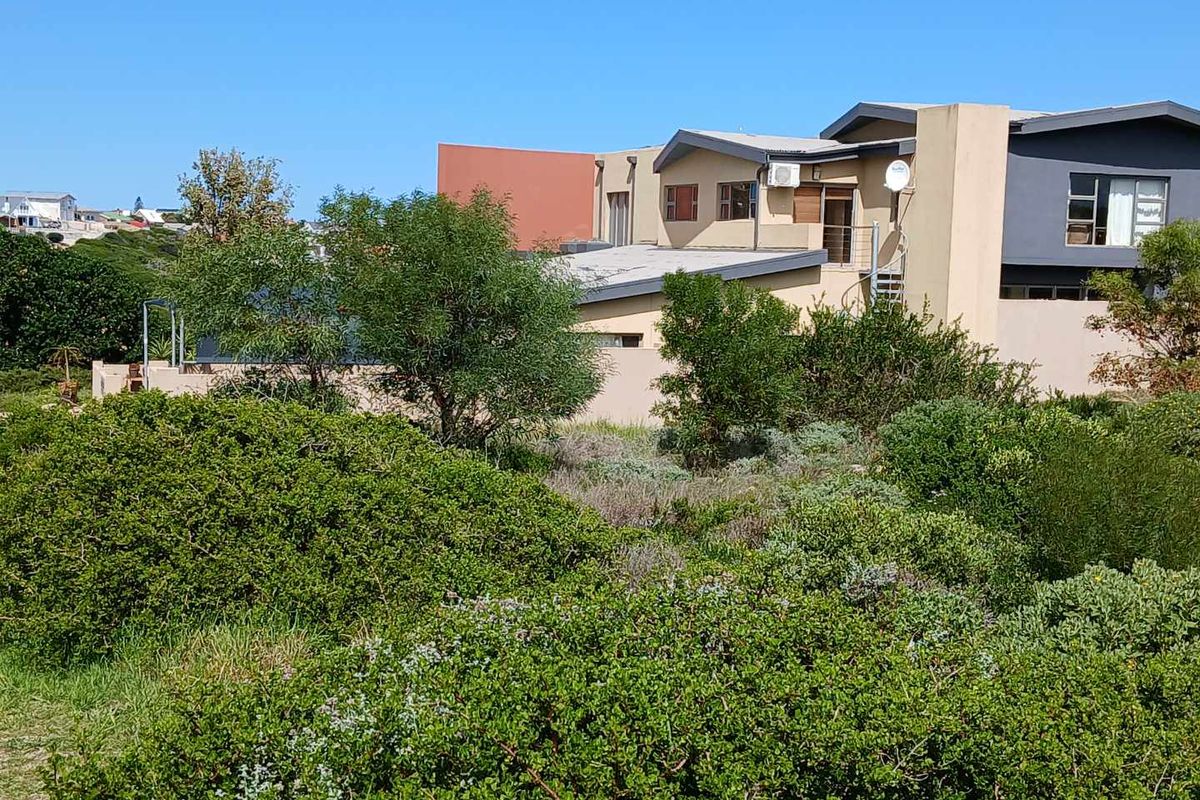 A view of the residential property from the adjacent vacant land, showcasing the exterior facade, roof structure, and surrounding natural vegetation.