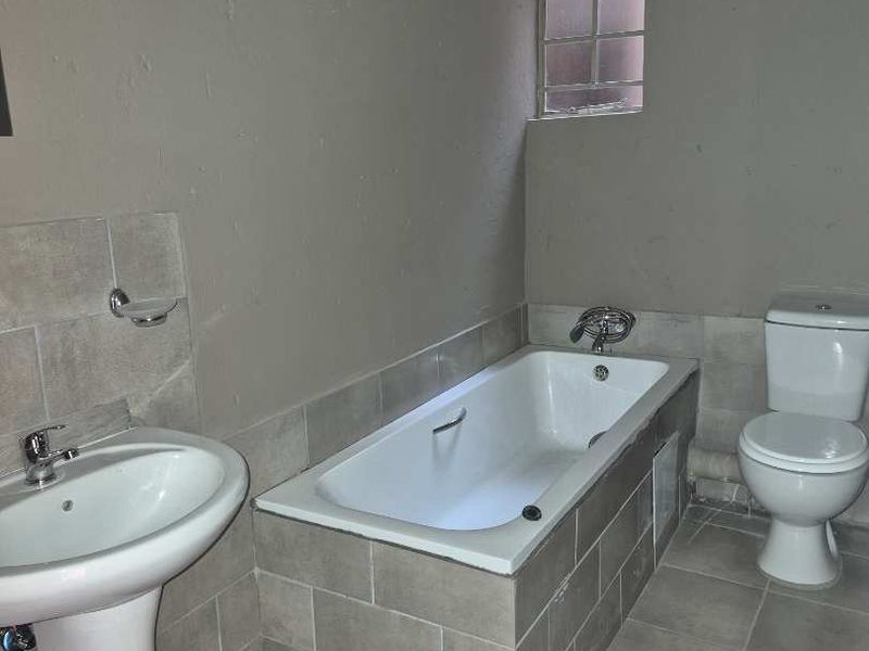 A functional bathroom featuring a pedestal basin, built-in bathtub, and toilet, with tiled finishes. The space requires ceiling completion and plumbing concealment.