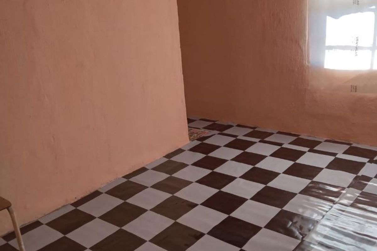 An empty living area featuring checkered vinyl flooring and plain peach-toned walls, offering a blank canvas for renovation and interior design updates.