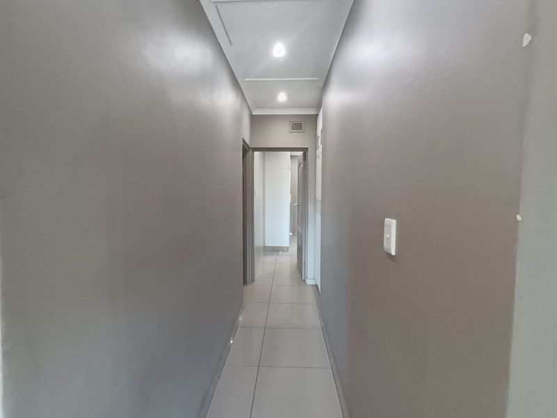 A clean, neutral-toned hallway featuring tiled flooring, recessed downlighting, and built-in storage cupboards, providing a functional transition space between rooms.