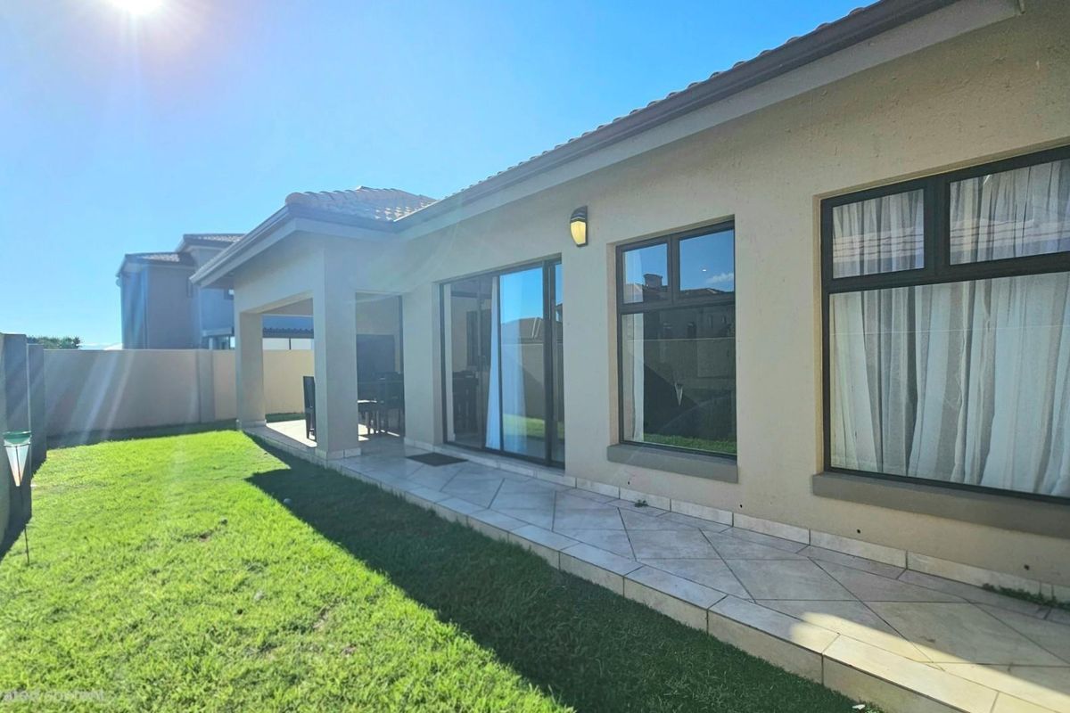 Rear view of the property featuring a tiled patio, sliding glass doors, and a well-maintained garden area.