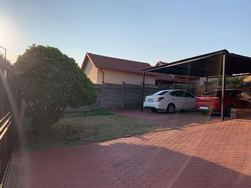 Front exterior view of the property featuring a paved driveway, a covered carport, and a secure boundary wall.
