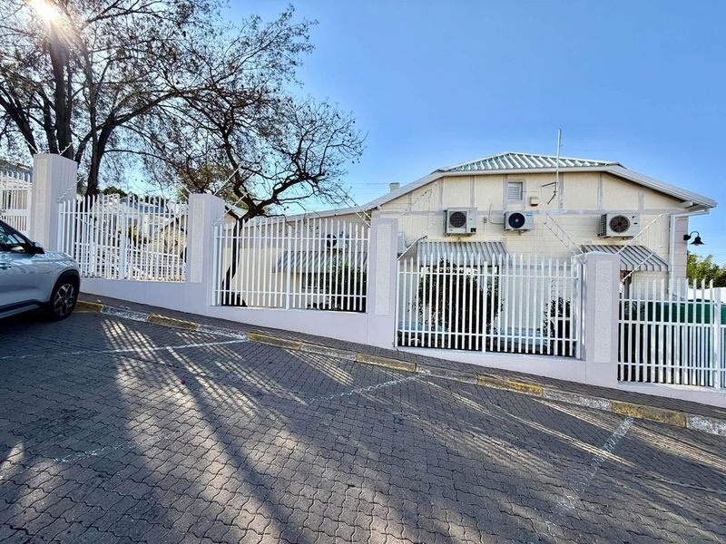 Front exterior view of the office property featuring secure perimeter fencing, paved driveway, and multiple external air conditioning units.