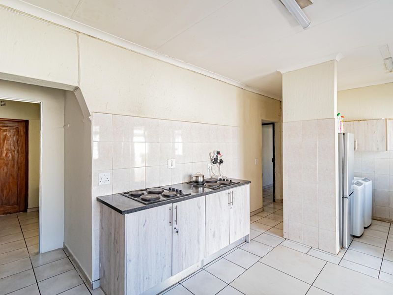 A functional kitchen area featuring built-in cabinetry, a hob, and tiled splashbacks, with an adjacent utility space visible.