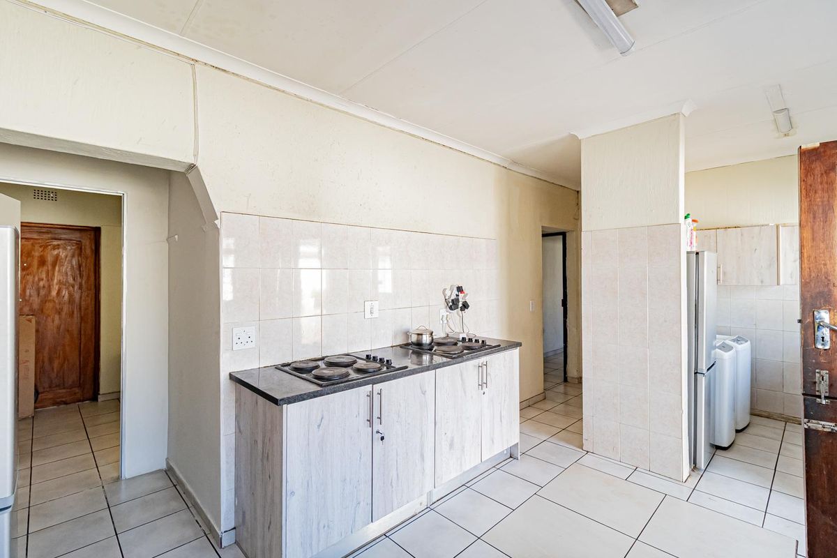 A functional kitchen area featuring built-in cabinetry, a hob, and tiled splashbacks, with an adjacent utility space visible.