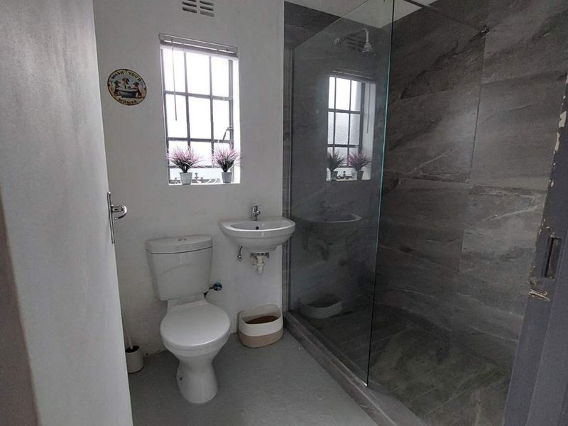 A modern bathroom featuring a walk-in shower with grey tiled walls, a wall-mounted basin, and a toilet.