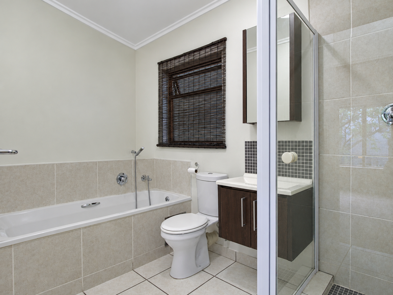 A clean, modern bathroom featuring a built-in bathtub, separate shower enclosure, vanity cabinet with mirror, and neutral tiled finishes throughout.