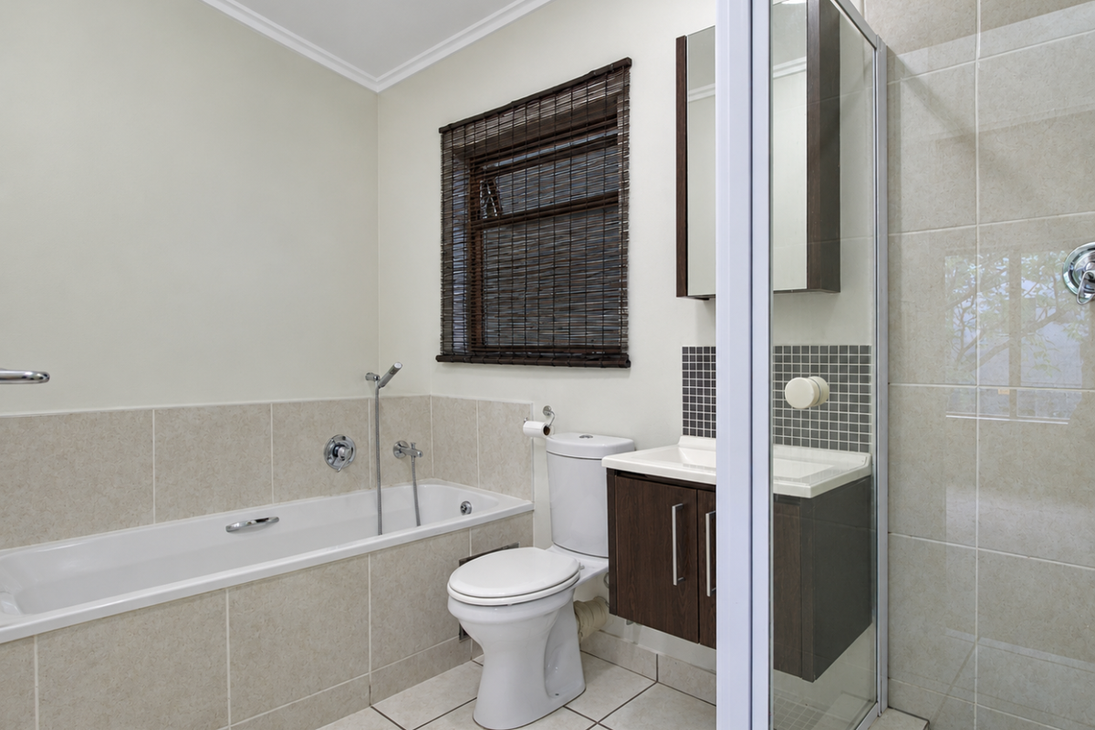 A clean, modern bathroom featuring a built-in bathtub, separate shower enclosure, vanity cabinet with mirror, and neutral tiled finishes throughout.