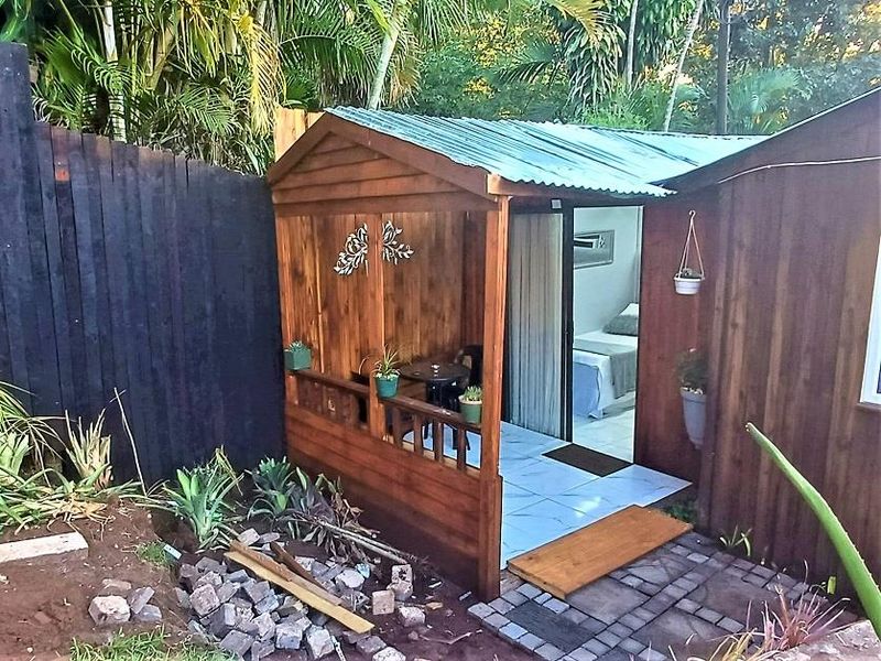 A covered timber patio area featuring tiled flooring and a sliding glass door entrance, set within a garden environment.