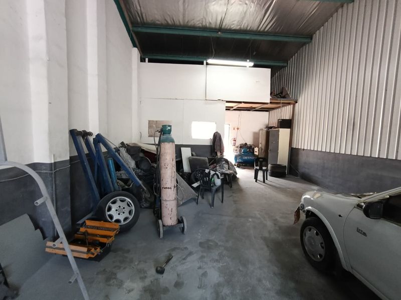 Industrial garage space featuring high ceilings with exposed steel trusses, concrete flooring, and a mezzanine storage level, suitable for workshop or storage use.