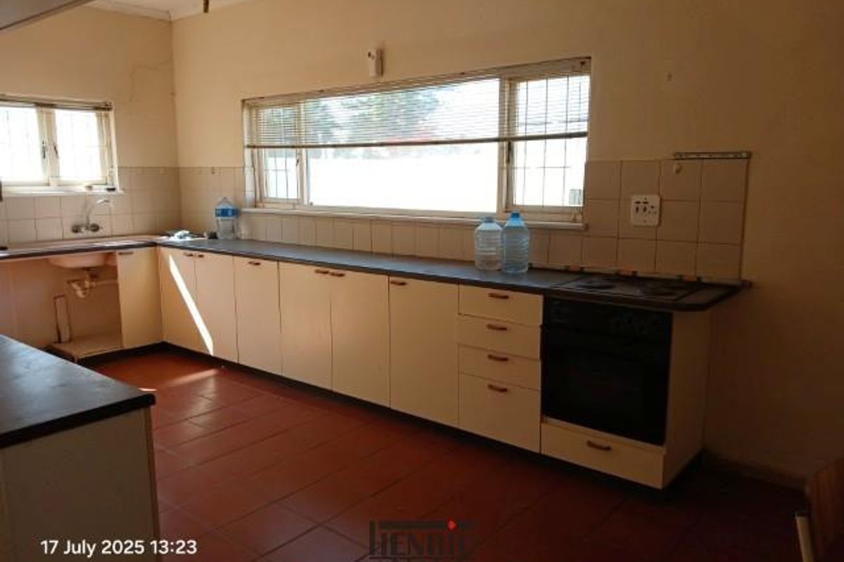 A dated kitchen featuring tiled flooring, laminate cabinetry, a built-in oven and hob, and a large window providing natural light.