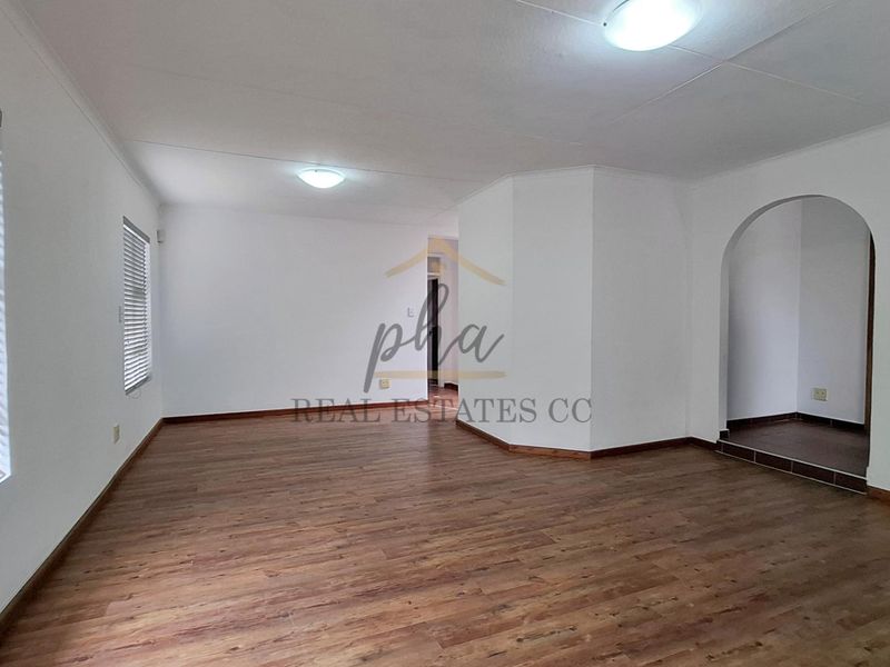 A spacious, empty living room featuring laminate wood flooring, white walls, and an arched entryway leading to an adjacent area.