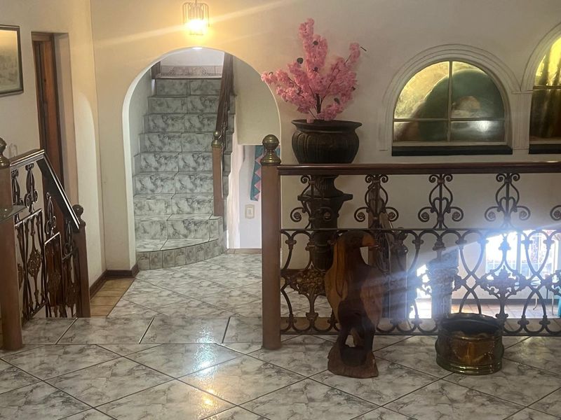 A tiled hallway featuring a decorative wrought iron balustrade, an arched staircase entrance, and an arched window, showcasing a traditional architectural style.