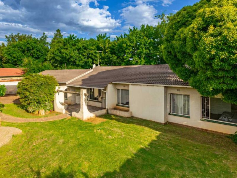Rear view of the house featuring a tiled roof, covered patio area, and a spacious garden with established trees.